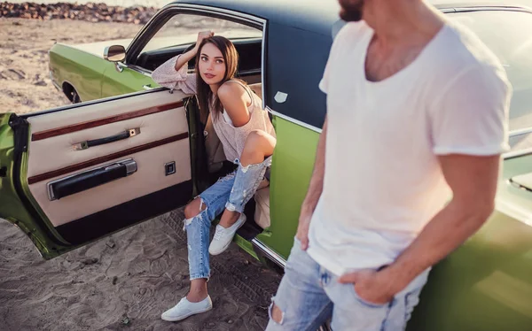 Romantik çift sahilde yeşil retro car yakınındaki duruyor. Sakallı yakışıklı ve çekici genç kadın eski model klasik araba. Aşk hikayesi.