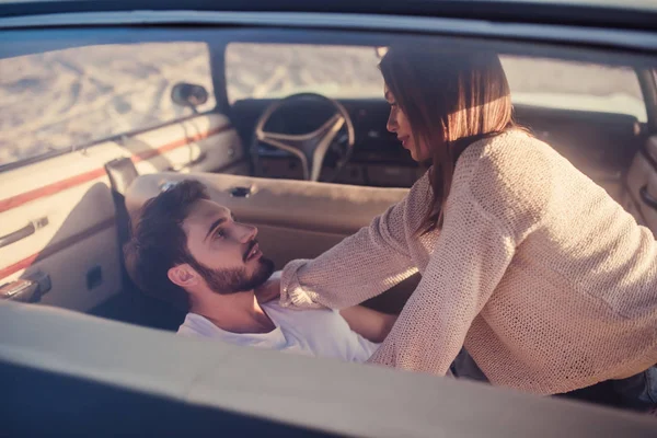 Romantik çift sahilde yeşil retro arabada oturuyor. Sakallı yakışıklı ve çekici genç kadın vintage klasik araba. Şık aşk hikayesi. Sarılma ve öpüşme arabaya olurken.
