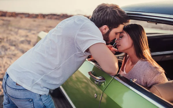 Romantik çift sahilde yeşil retro araba ile. Sakallı yakışıklı ve çekici genç kadın eski model klasik araba. Onu adam yakın duruyor ve onu öpecek şık kız arabada oturuyor. Aşk hikayesi.