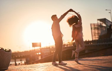 Love is in the air! Cute romantic couple spending time together in the city. Handsome bearded man and attractive young woman are in love. Dancing during sunset. clipart