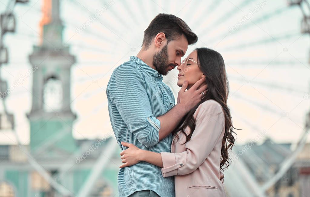 Love is in the air! Cute romantic couple spending time together in the city. Handsome bearded man and attractive young woman are in love. Hugging, kissing and having fun on the Ferris wheel background.