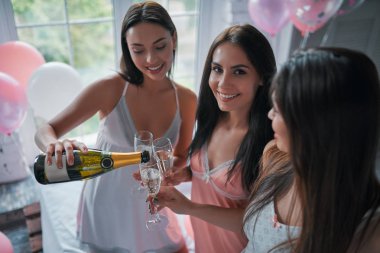 Üç genç çekici kadın evde yatak odasında eğleniyorlar. Kızların pijama partisi. Yatağa birlikte otururken şampanya içmek.