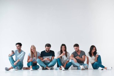 Bir grup genç insan beyaz arka plan üzerinde izole. Çekici gençlik elinde akıllı telefonlar ile birlikte oturuyor. Teknoloji kavramı.