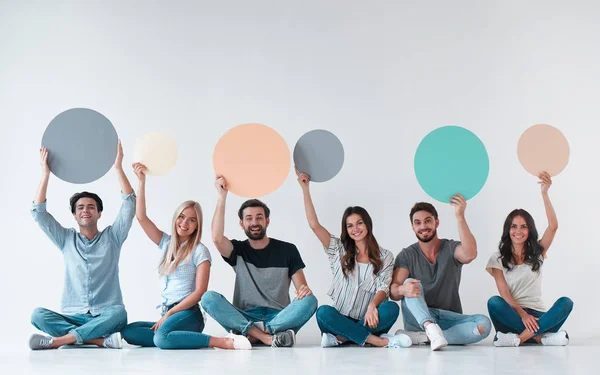 Group of young people isolated on white background. Attractive youth sitting together with empty circle advertisement boards.