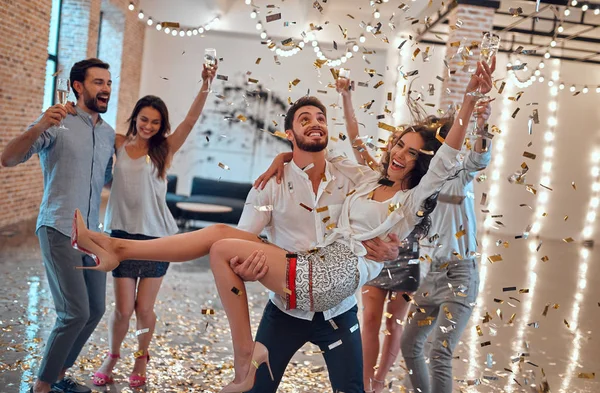 Let the party begin! Group of young people having fun together. Dancing in big light room with champagne and confetti falling. Celebrating holiday in big company of close friends.