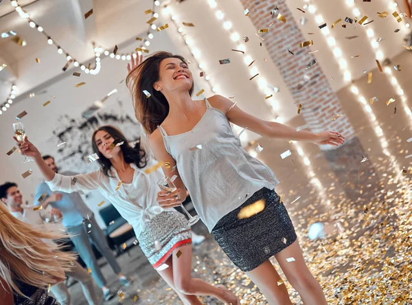 Let the party begin! Group of young people having fun together. Dancing in big light room with champagne and confetti falling. Celebrating holiday in big company of close friends.