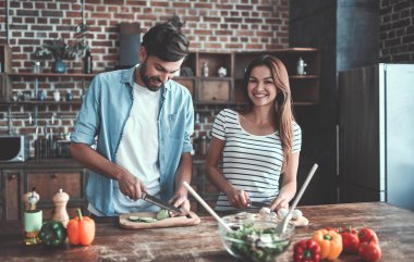 Romantik Çift mutfak yemek pişiriyor. Yakışıklı ve çekici genç kadın birlikte salata yaparken eğleniyor musun. Sağlıklı yaşam konsepti.