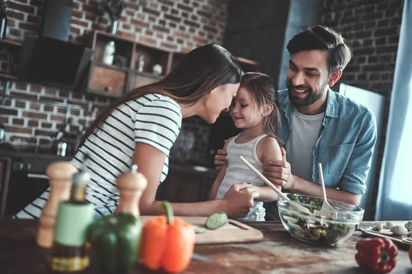 Mom, dad and daughter are cooking on kitchen. Happy family concept. Handsome man, attractive young woman and their cute little daughter are making salad together. Healthy lifestyle.