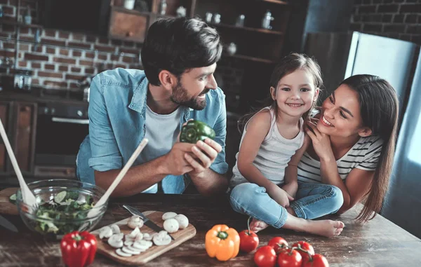 Mom, dad and daughter are cooking on kitchen. Happy family concept. Handsome man, attractive young woman and their cute little daughter are making salad together. Healthy lifestyle.
