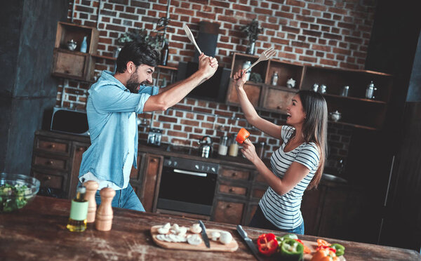 Romantic couple is cooking on kitchen. Handsome man and attractive young woman are having fun together while making salad. Healthy lifestyle concept.