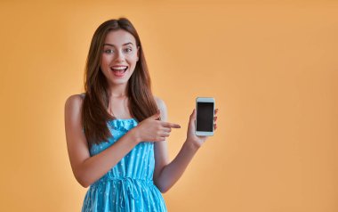 Çekici genç kadın üzerinde turuncu arka plan izole. Mutlu kız mavi elbiseli sarı arka plan Akıllı telefon ile poz.