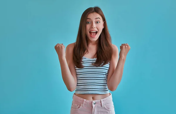 Attractive young woman isolated on blue background. Portrait of happy girl posing and rejoices. Victory!