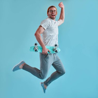 Yakışıklı adam izole. Gözlük şık genç adam kaykay üzerinde mavi arka plan ile poz.