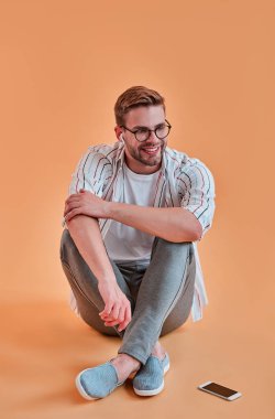 Yakışıklı adam izole. Gözlük şık genç adam akıllı telefon turuncu arka plan ile poz. Kablosuz kulaklık kullanarak müzik