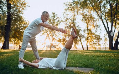 Üst düzey çift açık havada spor yapıyor. Parkta gündoğumu sırasında germe. Birlikte yoga yapıyor. Sağlıklı yaşam konsepti