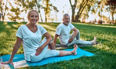 Üst düzey çift açık havada spor yapıyor. Parkta gündoğumu sırasında germe. Birlikte yoga yapıyor. Sağlıklı yaşam konsepti