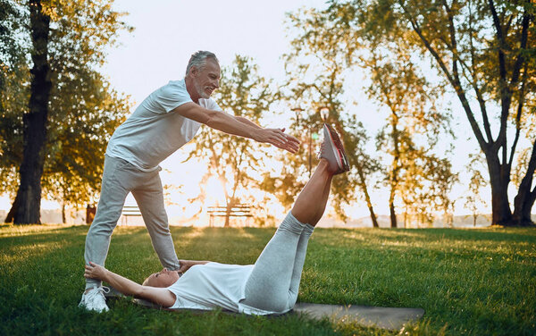 Senior couple is doing sport outdoors. Stretching in park during sunrise. Doing yoga together. Healthy lifestyle concept