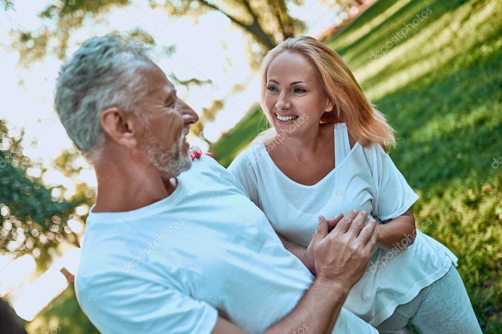 Senior couple is spending time together outdoors. Bearded handsome man and attractive woman are hugging while being in park.