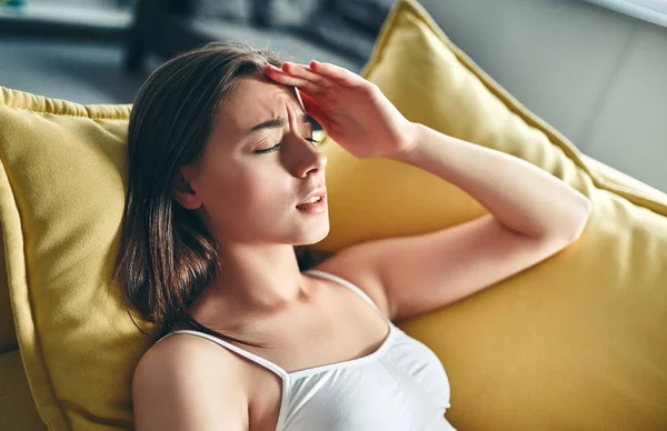 Good morning! Attractive young woman is having rest at home. Girl lying on sofa and experiencing headache.