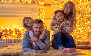 Mutlu Noeller ve mutlu yeni yıl! Mutlu aile kutluyor kış tatili evde. Anne, Baba, kızı ve oğlu Noel için dekore edilmiş yeni yıl ağacı yanında otururken bekliyor.