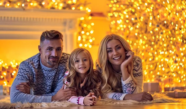 Merry Christmas and Happy New Year! Happy family celebrating winter holiday at home. Mother, father and daughter are waiting for Christmas while lying near decorated New Year tree.