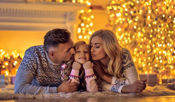 Merry Christmas and Happy New Year! Happy family celebrating winter holiday at home. Mother, father and daughter are waiting for Christmas while lying near decorated New Year tree.