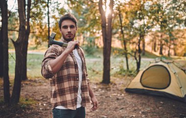 Male tourist exploring new places. Handsome bearded man on nature. Man with ax and firewood near touristic tent. Lumberjack clipart