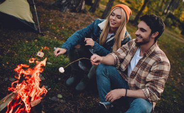 Turist genç çift yeni yerler keşfediyoruz. Çekici kadın ve yakışıklı adam birlikte doğa üzerinde vakit. Şenlik ateşi ve orman ve hatmi yapmak turistik çadırda yakın oturan.