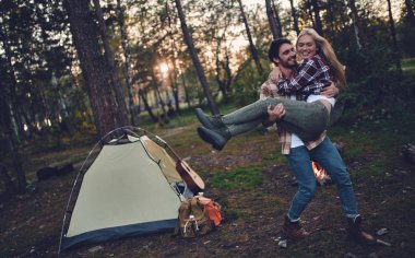 Genç çift turist birlikte yeni yerler keşfetme eylemi. Çekici genç kadın ve yakışıklı sakallı adam birlikte doğa üzerinde vakit. Şenlik ateşi ve orman turistik çadırın yakınında duran.