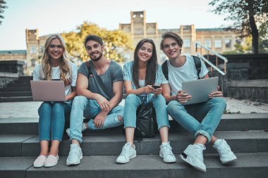 Bir grup genç insan ders birlikte üniversitede. Açık havada merdivenlerde oturan öğrenciler.