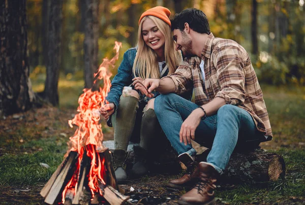 年轻的一对游客正在探索新的地方 有魅力的女人和英俊的男人都在大自然上呆着 坐在篝火和森林中的旅游帐篷附近 制作棉花糖 — 图库照片