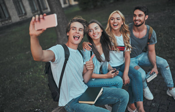 Group of young people are studying together in university. Students outdoors making selfie on a smart phone.