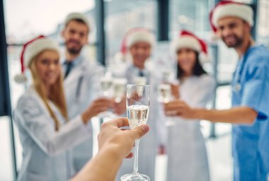 Mutlu Noeller ve mutlu yeni yıl! İş yerinde kış tatilleri kutluyor doktorlar grubu. Üniforma ve Noel Baba şapkaları birlikte şampanya içmek sağlık personeli.