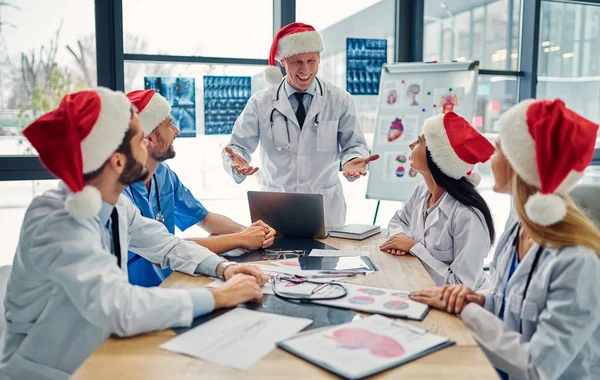 Merry Christmas and Happy New Year! Group of doctors celebrating winter holidays together at work. Medical personnel in uniform and Santa Claus hats.