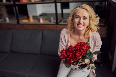 Çekici kadın kıdemli kırmızı gül demet ile evde kanepede oturuyor.