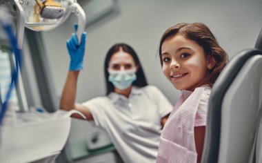Diş kliniğindeki tatlı kız. Kadın dişçi ile stomatoloji kabinesindeki çocuk.