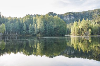 Çek Cumhuriyeti 'nin Avrupa' daki Hradec Kralove Bölgesi 'ndeki Adrspach-Teplice Kayalıkları bölgesinde bulunan Piskovna Gölü. Berrak, berrak bir gökyüzünün altında bereketli ormanı ve kaya oluşumlarını yansıtan huzurlu göl..