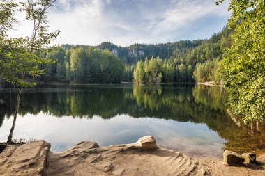Adrspach-Teplice Kayalıkları 'ndaki Piskovna Gölü, Çek Cumhuriyeti' nin Hradec Kralove Bölgesi, Avrupa. Sakin, güneşli bir günde, sakin bir ormanla çevrili sakin bir göl, sakin sudaki ağaçları yansıtıyor..