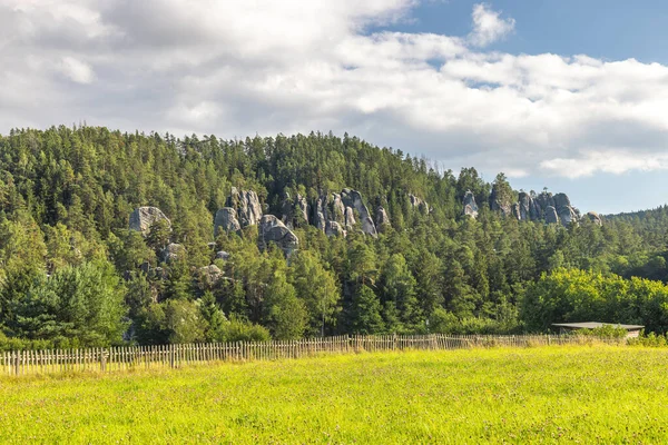 Çek Cumhuriyeti 'nin Avrupa' daki Hradec Kralove Bölgesi 'ndeki Adrspach-Teplice Kayalıkları' nın manzarası. Bereketli bir çayır, ahşap çit, ormanla kaplı tepe, kaya oluşumları içeren manzaralı bir yer..