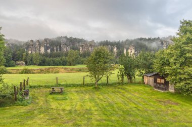 Çek Cumhuriyeti 'nin Avrupa' daki Hradec Kralove Bölgesi 'ndeki Adrspach-Teplice Kayalıkları' nın manzarası. Bulutlu bir günde sisli, tarlada ve kırsal alanda gizlenmiş kaya oluşumları olan manzaralı bir yer..