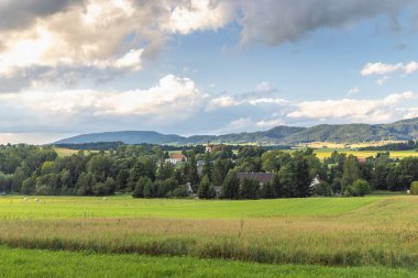 Avrupa 'nın Çek Cumhuriyeti' nin Hradec Kralove bölgesindeki Broumovsko Koruma Alanı. Yeşil tarlalar, ağaçlar, yuvarlanan tepeler ve bulutlu bir gökyüzünün yer aldığı manzara..
