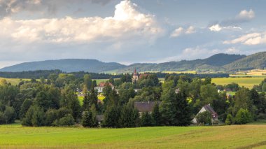 Avrupa 'nın Çek Cumhuriyeti' nin Hradec Kralove bölgesindeki Broumovsko Koruma Alanı. Yeşilliklerin arasına yerleşmiş bir köyün yer aldığı manzaralı bir kır manzarası.