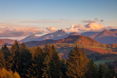 Ağaçları ve tepeleri, mavi bulutlu gökyüzüne doğru aydınlatan ılık ışık saçan sonbahar manzarası. Slovakya, Avrupa 'daki Mala Fatra Milli Parkı.