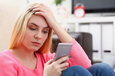 Genç sarışın womansit kanepe tutun Smartphone elinde güzel