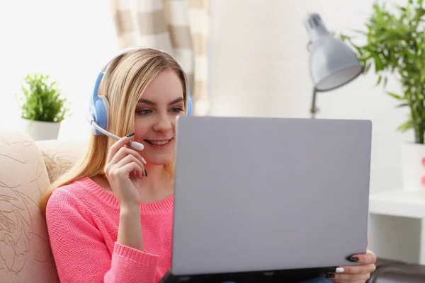 年轻美丽的金发女人坐在沙发上客厅里拿着手提电脑在胳膊听音乐 — 图库照片