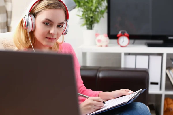 Jovem bela mulher loira sentar-se no sofá na sala de estar segurar aglutinante no trabalho de armas com laptop ouvir música — Fotografia de Stock