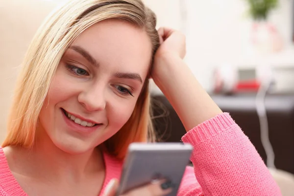 Jovem bonita loira womansit no sofá segurar smartphone em mãos — Fotografia de Stock