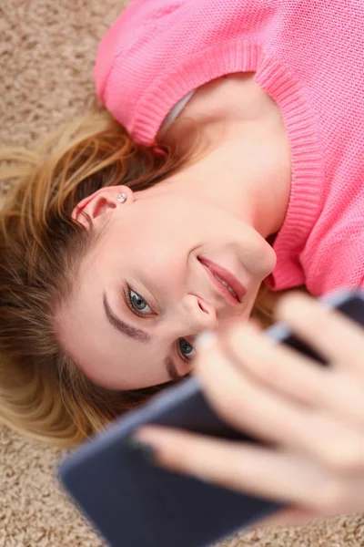 Jovem bela mulher tem um descanso mentira no chão segurar smartphone nos braços — Fotografia de Stock