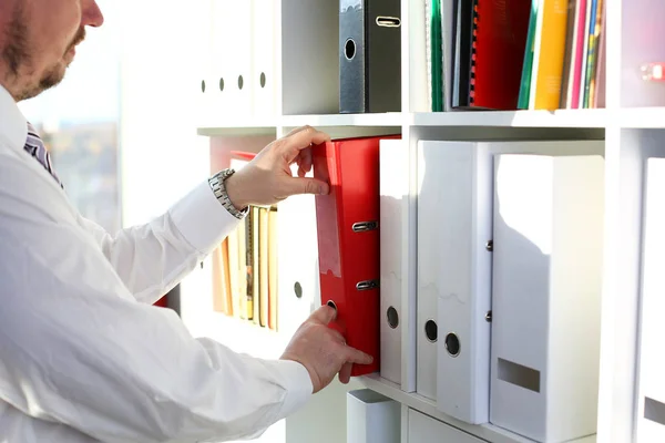 Male arms pick red file folder from office book shelf — Stock Photo, Image