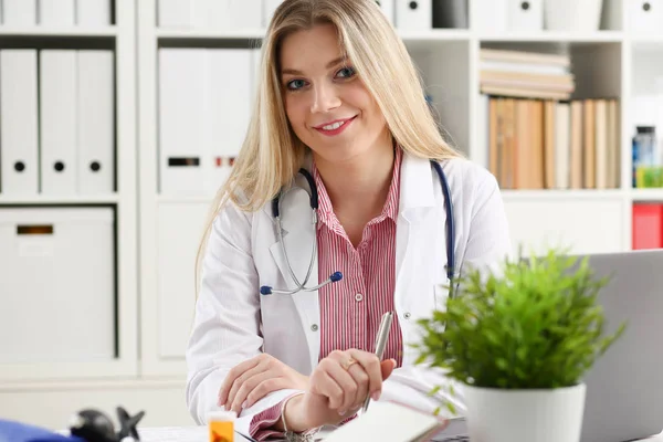 Hermosa mujer sonriente médico sentarse en el lugar de trabajo —  Fotos de Stock